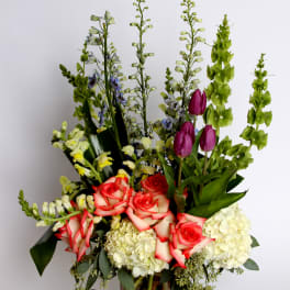 Tall mixed bouquet with roses, hydrangeas, and purple tulips in a glass vase
