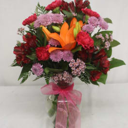Bouquet of orange lilies and pink-red flowers in a glass vase with a pink ribbon