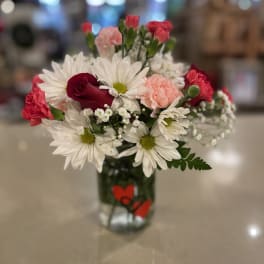 Bouquet of white daisies, red roses, and pink carnations in a glass vase