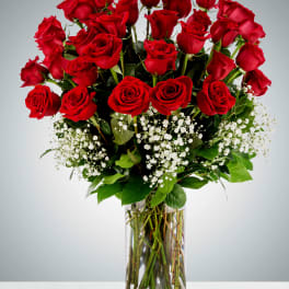 Tall arrangement of red roses and white filler flowers in a clear glass vase