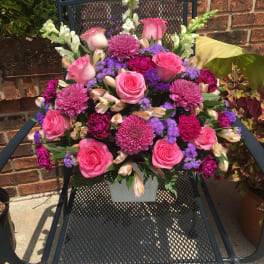 Pink and purple mixed flower arrangement in a white container