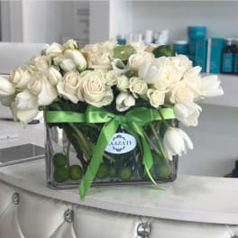 White roses and tulips arranged in a glass vase with a green ribbon.