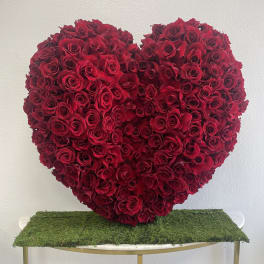 Heart-shaped arrangement of red roses on a moss-covered table