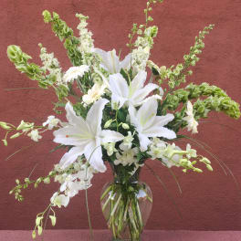 White lilies and orchids arranged in a clear glass vase