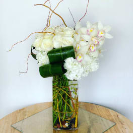 White roses and orchids arranged in a tall glass vase