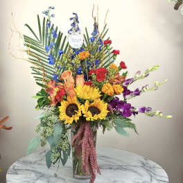 Tall mixed bouquet in a glass vase with sunflowers, orchids, and carnations