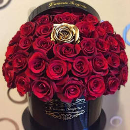 Round black hatbox filled with red roses and a single gold rose in the center