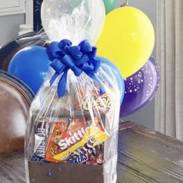 Gift basket of candy with colorful balloons and a blue bow
