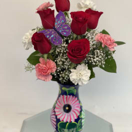 Red roses and pink carnations in a painted vase with a purple butterfly decoration