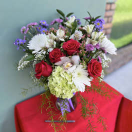 Bouquet of red roses, white blooms, and purple flowers in a vase
