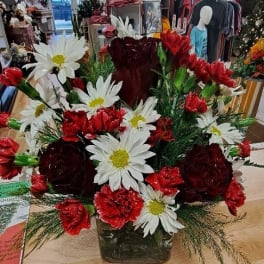 Red carnations and white daisies arranged in a square glass vase.