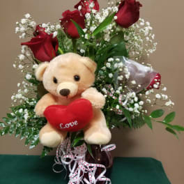 Red roses with a teddy bear holding a heart in a glass vase