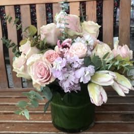 Pink and cream roses with pale purple flowers in a green vase