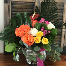 Colorful rose bouquet in a glass vase with tropical leaves