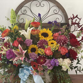Large mixed flower arrangement with sunflowers, roses, lilies, and a blue ribbon