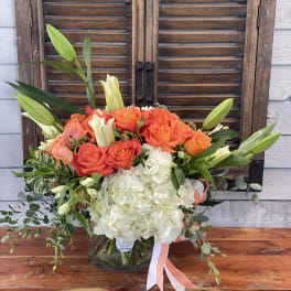 Bouquet of orange roses, white hydrangeas, and lilies in a glass vase