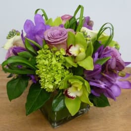 Purple and green floral arrangement in a square glass vase