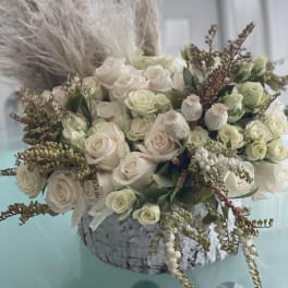 Cream roses arranged in a low stone vase with dried grasses