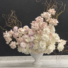 Large asymmetrical arrangement of blush and white flowers in a white urn