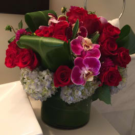 Red roses and purple orchids in a green vase with pale hydrangeas
