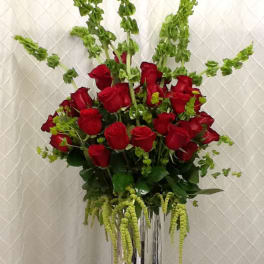 Red roses arranged in a tall silver vase with green filler flowers