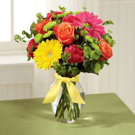 Mixed bouquet of bright flowers in a clear glass vase with a yellow ribbon