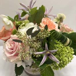 Short arrangement of peach and pink roses with white and green blooms in a clear glass vase