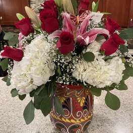 Red roses and pink lilies arranged with white blooms in a painted vase.