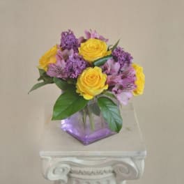 Yellow roses and purple flowers in a square glass vase