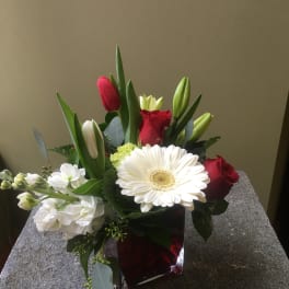 Mixed bouquet with red roses, white gerbera daisy, and tulips in a red vase