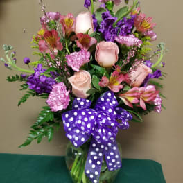 Pink and purple mixed bouquet in a glass vase with a polka-dot ribbon