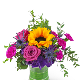 Mixed bouquet with yellow sunflower, purple rose, hot pink carnations, and blue thistle in a glass vase
