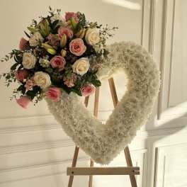 Heart-shaped white floral wreath with pink roses on a wooden easel