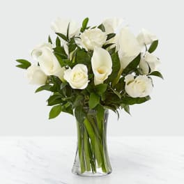 Arrangement of white roses and white calla lilies in a clear glass vase