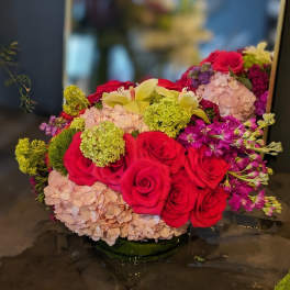 Bouquet of red roses, pale hydrangeas, and yellow lilies in a low glass vase
