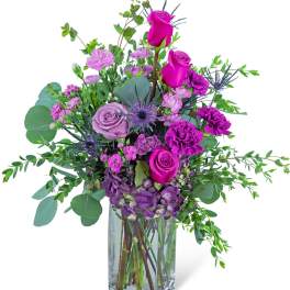 Tall arrangement of purple and hot pink roses and carnations in a clear glass vase