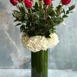 Red roses arranged in a tall glass vase with white hydrangeas at the base.