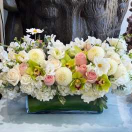 Low floral arrangement of white blooms, pink roses, and green orchids in a glass vase