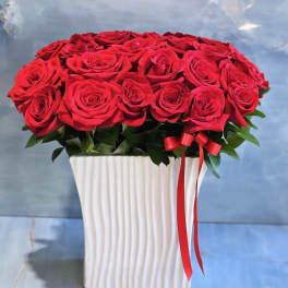 Red roses arranged in a white square vase with a red ribbon