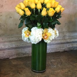 Yellow roses and white orchids arranged in a tall green vase