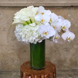 White floral arrangement with orchids, hydrangeas, and calla lilies in a green vase