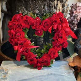 Heart-shaped arrangement of red roses with ribbon accents