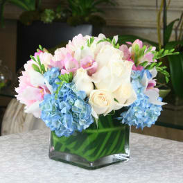 Pink and white bouquet with blue hydrangeas in a square glass vase