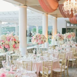 Pink and white floral centerpieces on round banquet tables with gold chairs