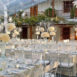 White floral centerpieces on long banquet tables at an outdoor event.