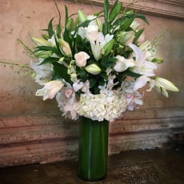 White lilies and pale pink roses in a tall green vase