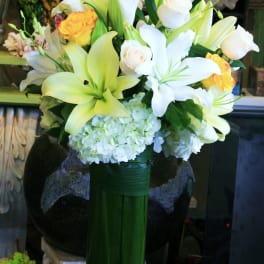 Bouquet of white lilies, white roses, and yellow roses in a tall green vase