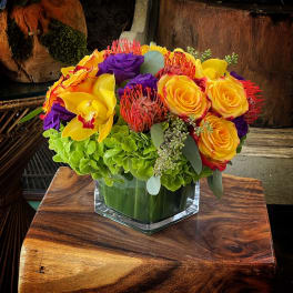 Bright bouquet of yellow roses, purple blooms, and orchids in a glass vase