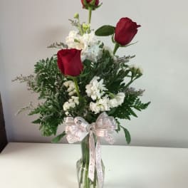 Red roses and white flowers in a clear glass vase with a ribbon bow
