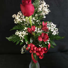 Red rose and alstroemeria bouquet in a glass vase with a red ribbon